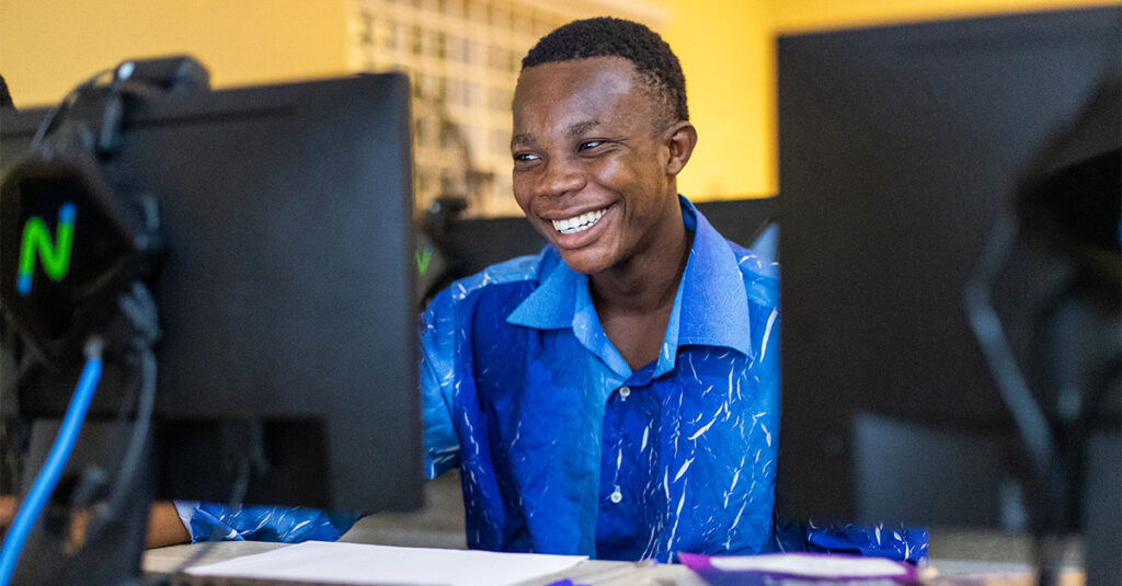 A young African boy smiling at a computer screen